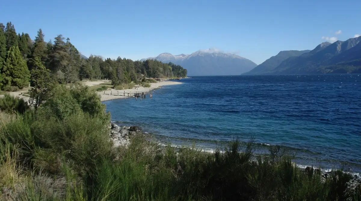 Playa y muelle de Villa Traful sobre el lago, con la cordillera nevada al fondo